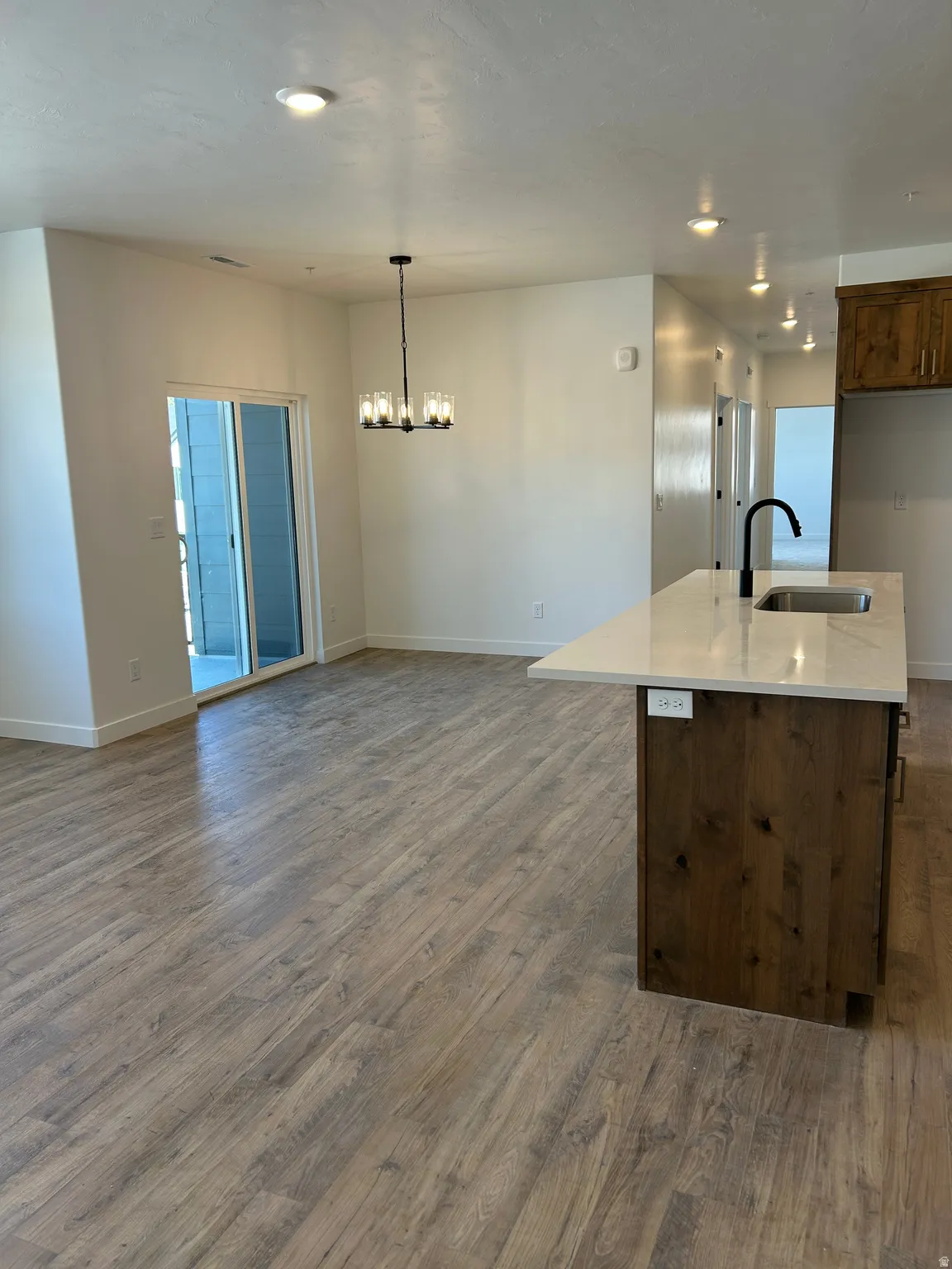 Wood-finish flooring throughout, kitchen island with a light-toned countertop, black gooseneck faucet, and stainless steel sink