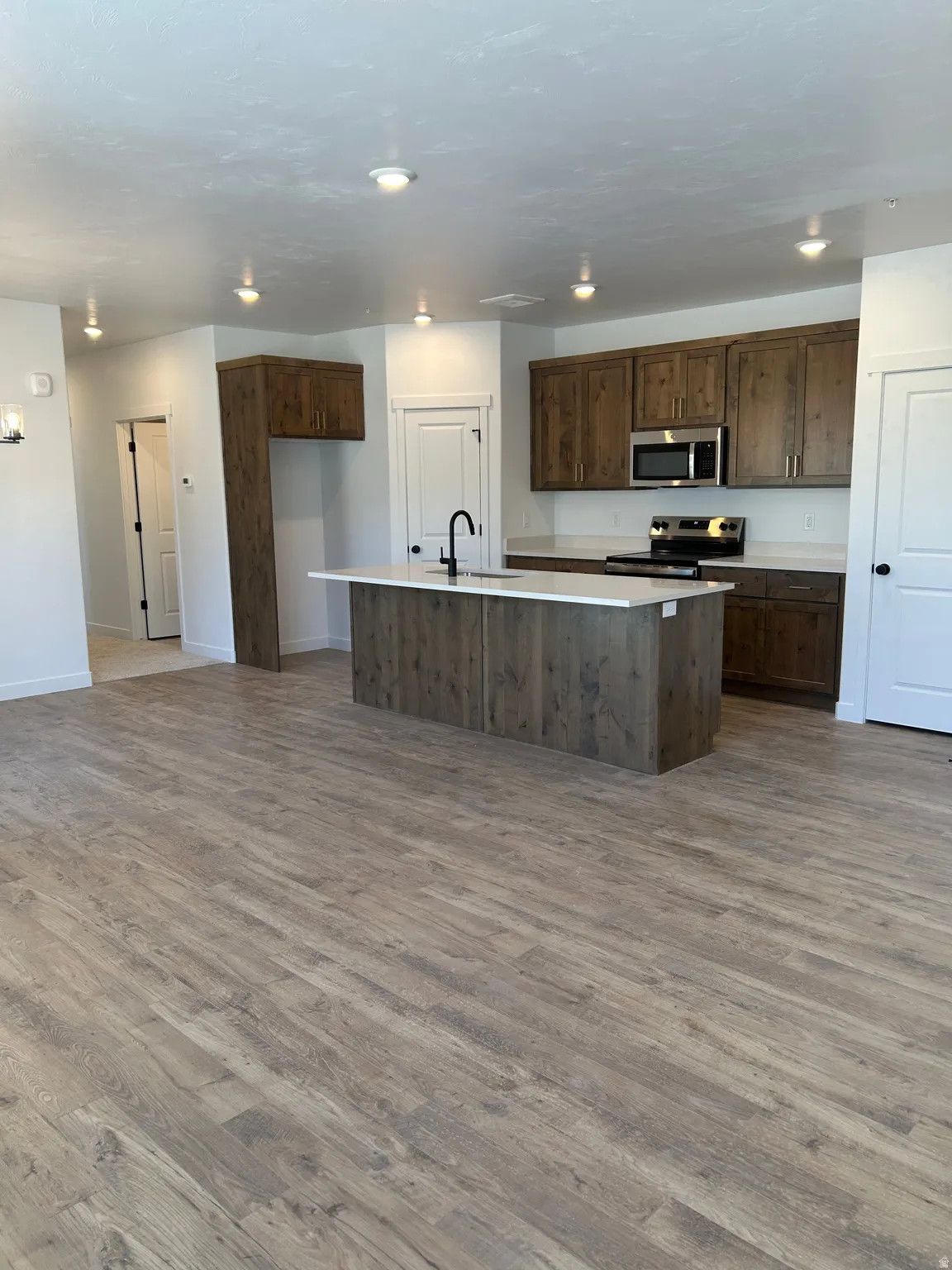 Kitchen island with integrated sink, wood-finish flooring, recessed ceiling lighting, wood-finish cabinetry, and stainless steel appliances