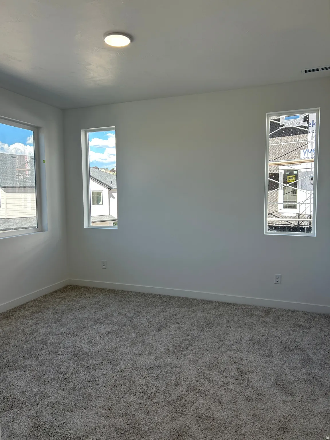 Plush gray carpeting, multiple windows providing ample natural light, clean white walls, recessed ceiling light fixture, and contemporary white trim