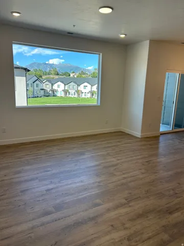 Expansive window with mountain scenery, recessed ceiling lighting, wood-finish flooring, white baseboards, and a sliding glass door