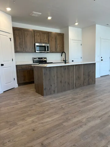 Kitchen featuring wood-finish cabinetry, stainless steel appliances, a center island with a white countertop, a matte black faucet, and wood-finish flooring