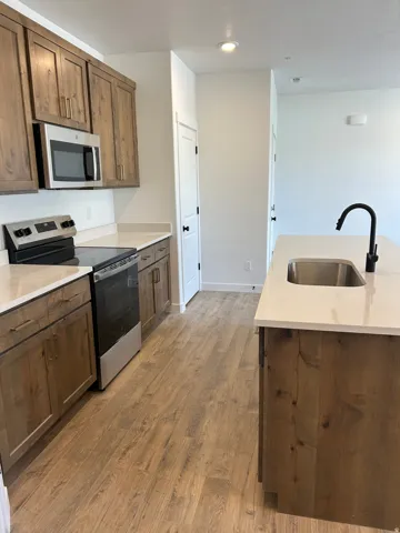 Modern kitchen featuring wood-finish cabinetry, light-toned countertops, stainless steel appliances, and wood-finish flooring