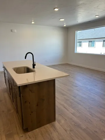 Kitchen island with integrated sink, black gooseneck faucet, light-toned countertop, and wood-finish cabinetry