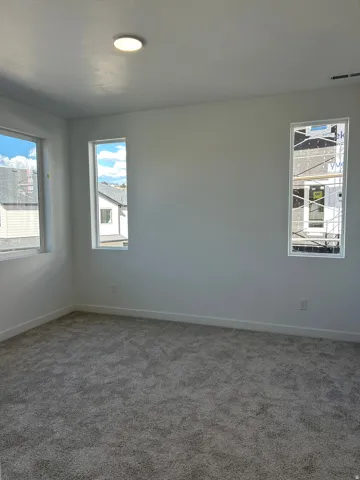 Plush gray carpeting, multiple windows providing ample natural light, clean white walls, recessed ceiling light fixture, and contemporary white trim