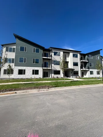 Multi-story building featuring a modern architectural design with a sloped roofline, balconies, and a mix of siding and stone veneer