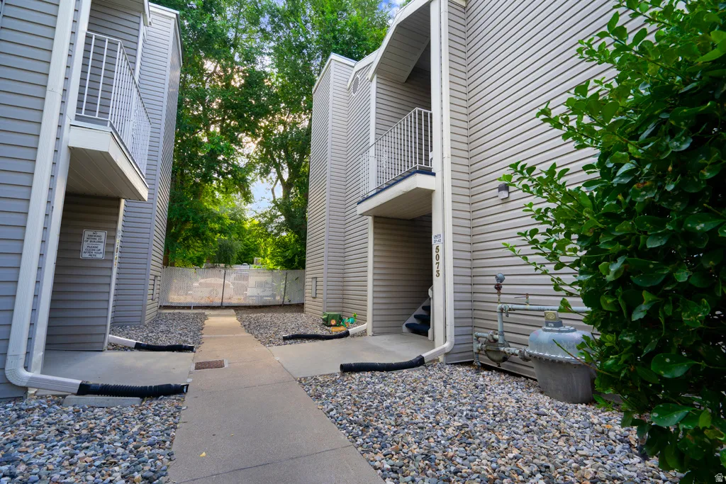 Exterior siding with individual balconies, a concrete pathway, and gravel landscaping