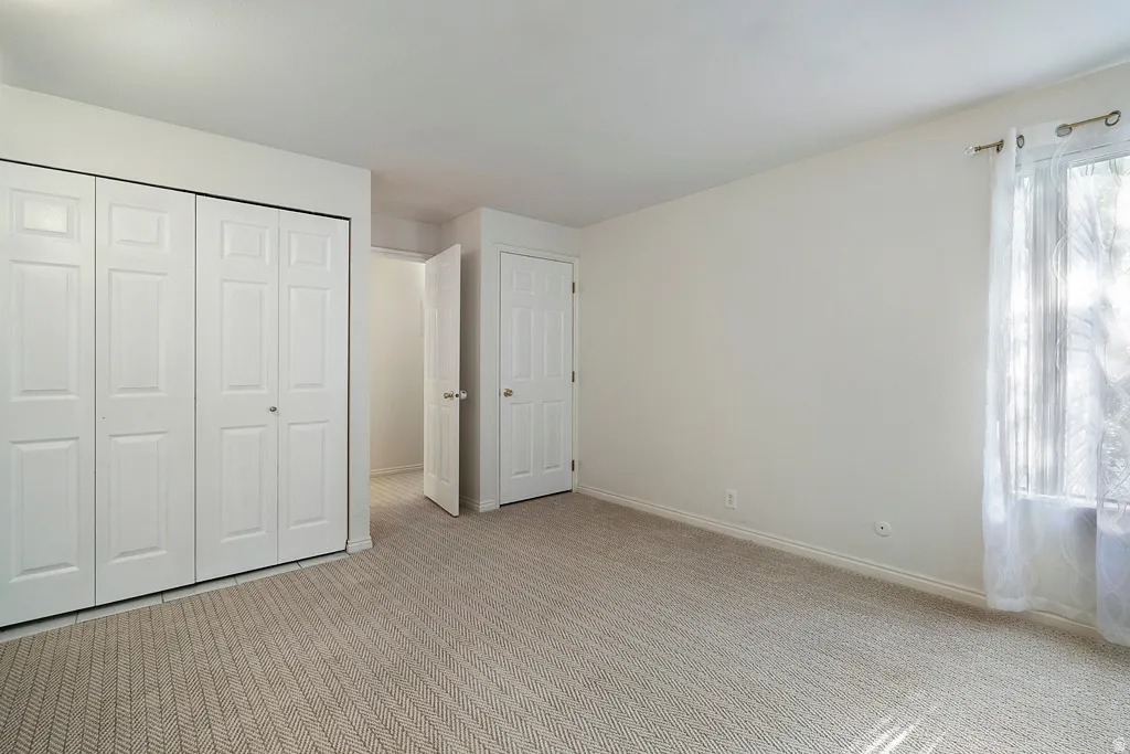 Textured carpet flooring, white bi-fold closet doors, white paneled interior doors, and a window with sheer curtains