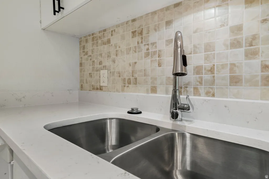 Dual stainless steel sink with a high-arch faucet, white countertops, and a mosaic tile backsplash