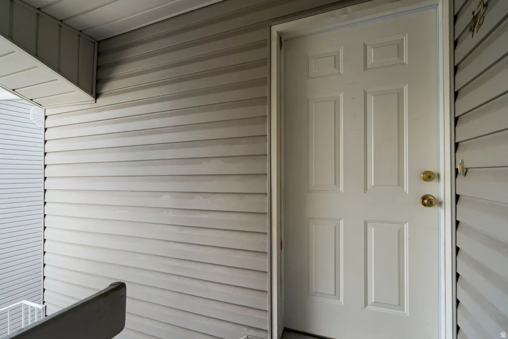White paneled entry door with brass hardware, surrounded by horizontal siding
