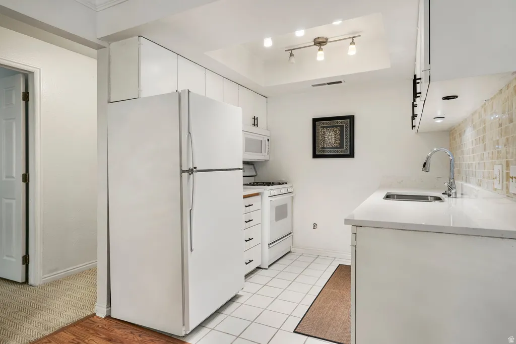 White kitchen cabinetry, solid surface countertops, square tile flooring, stainless steel sink with gooseneck faucet, and track lighting