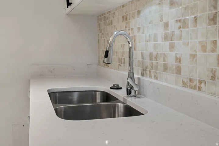 Dual basin stainless steel sink with a chrome pull-down faucet, set into a light-toned countertop, complemented by a tiled backsplash