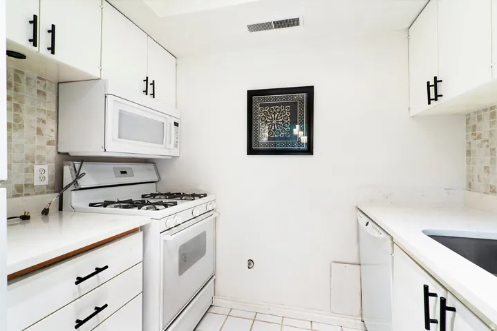 White cabinetry with black hardware, mosaic tile backsplash, white countertops, built-in microwave, and tile flooring