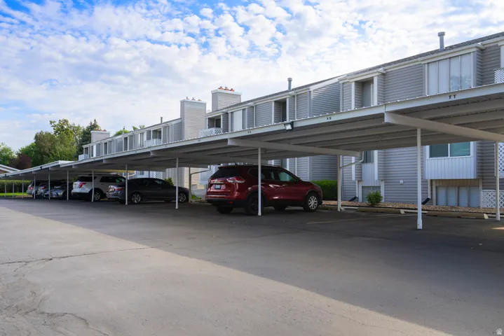 Covered parking structure with multiple spaces, featuring a light-colored metal frame and asphalt pavement