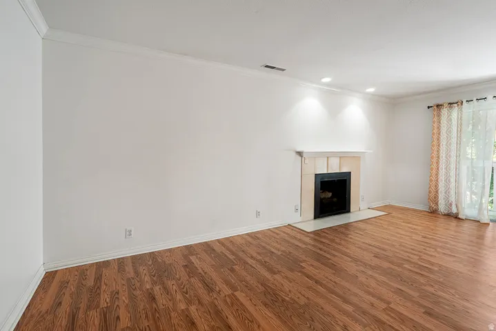 Wood-finish flooring, crown molding, recessed lighting, and a fireplace with a stone surround