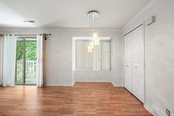 Wood-finish flooring, sliding glass door to a balcony, modern chandelier, window with vertical blinds, and bifold closet doors