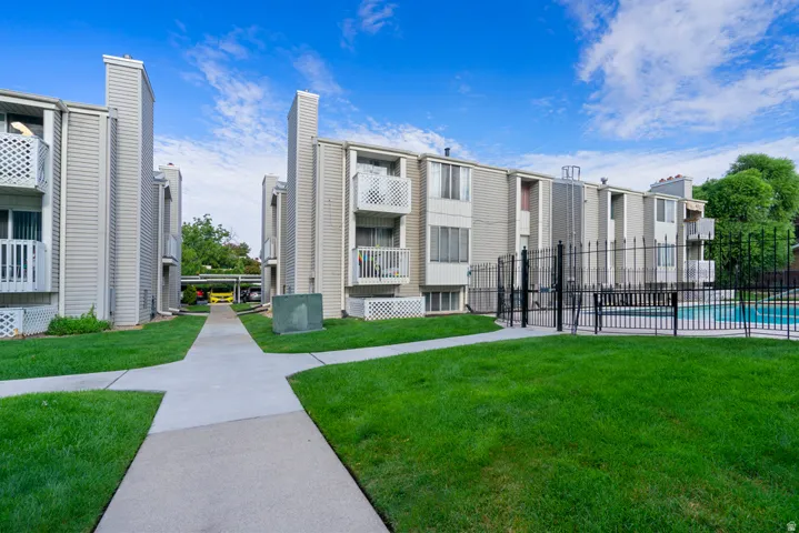Manicured green lawn with concrete walkways, fenced swimming pool, and multi-story buildings featuring balconies
