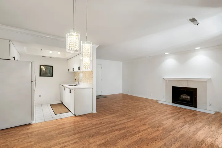 Wood-finish flooring, white cabinetry, a tiled kitchen area, and a fireplace with a stone surround