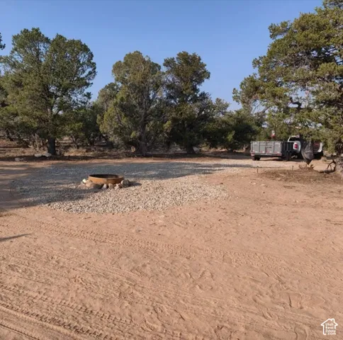 Outdoor area featuring a gravel pad with a fire pit, surrounded by mature trees