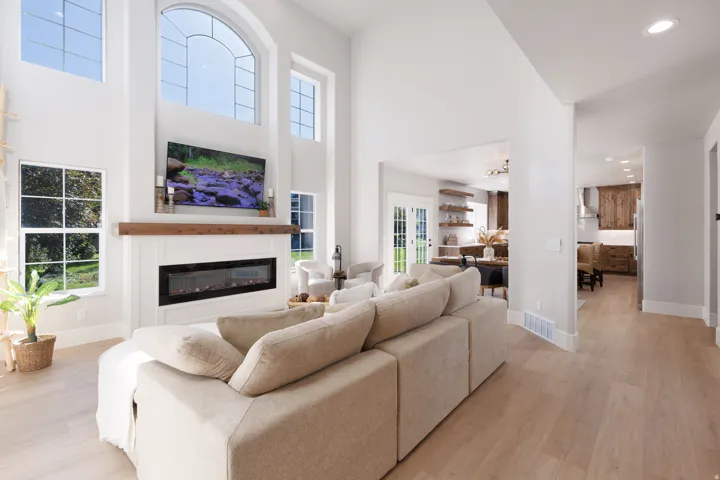 Soaring ceilings, a floor-to-ceiling fireplace with a wood-beam mantel, an arched window, and wood-finish flooring