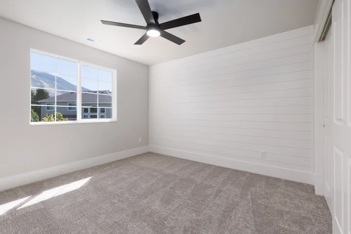 Textured carpet flooring, white shiplap accent wall, modern ceiling fan with integrated lighting, white trim work, and a multi-pane window