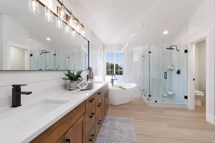 Dual vanity with white countertops, wood-finish cabinetry, a freestanding soaking tub, a glass-enclosed shower, and wood-finish flooring
