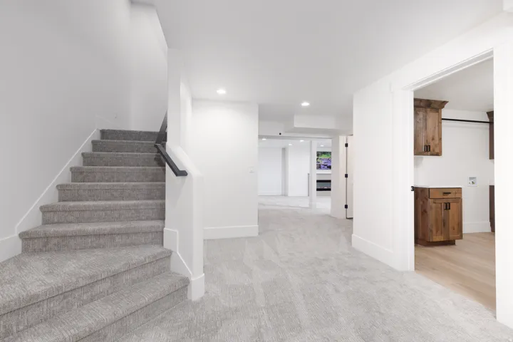 Carpeted staircase with dark handrail, recessed lighting, wood-finish cabinetry, and light wood-finish flooring