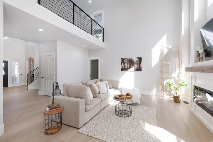 Spacious living area featuring high ceilings, wood-finish flooring, an open-concept loft with metal railing, and a built-in electric fireplace with a wood mantel