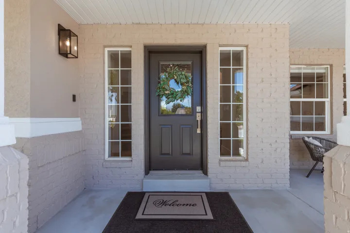 Brick exterior with painted finish, covered porch, dark entry door with window, sidelight windows, and outdoor sconce lighting
