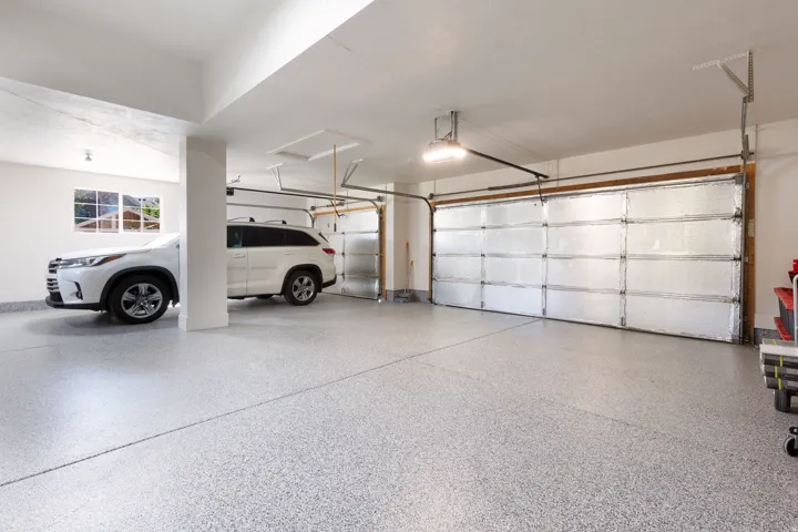 Spacious garage featuring a durable speckled epoxy floor finish, multiple overhead garage doors, and recessed lighting
