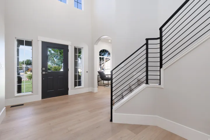 Foyer with high ceilings, light wood-finish flooring, and a dark entry door with glass panels