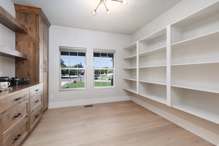 Built-in wood-finish cabinetry with matte black hardware, integrated shelving, light wood-finish flooring, and two double-hung windows