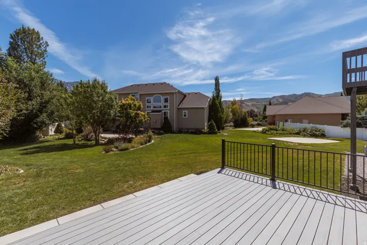 Spacious backyard with a composite deck, black metal railing, expansive lawn, and mature trees
