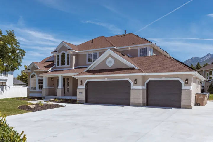 Stucco exterior with stone accent, concrete driveway, two-car garage, covered entry, and pitched shingle roof