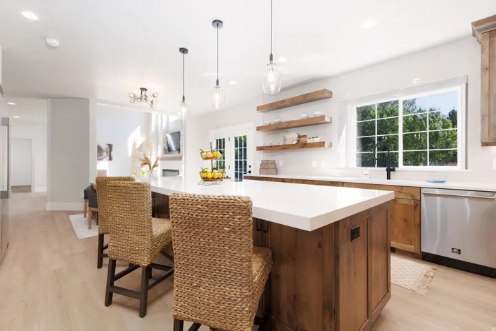 Kitchen featuring a large island with counter seating, light-toned wood-finish flooring, white countertops, built-in wooden shelving, and stainless steel appliances