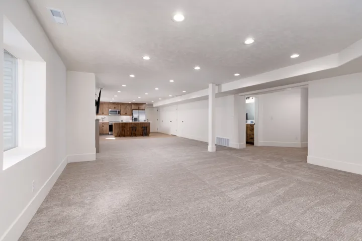 Spacious open-concept room featuring recessed lighting, light-toned carpeting, and a visible kitchen area with warm wood-finish cabinetry and a central island