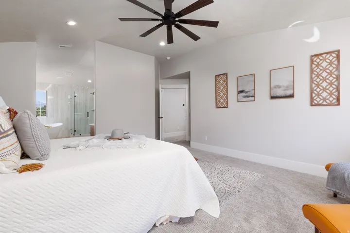 Recessed ceiling lighting, ceiling fan with dark wood-finish blades, light gray carpeting, and a built-in wall niche leading to an adjacent bathroom
