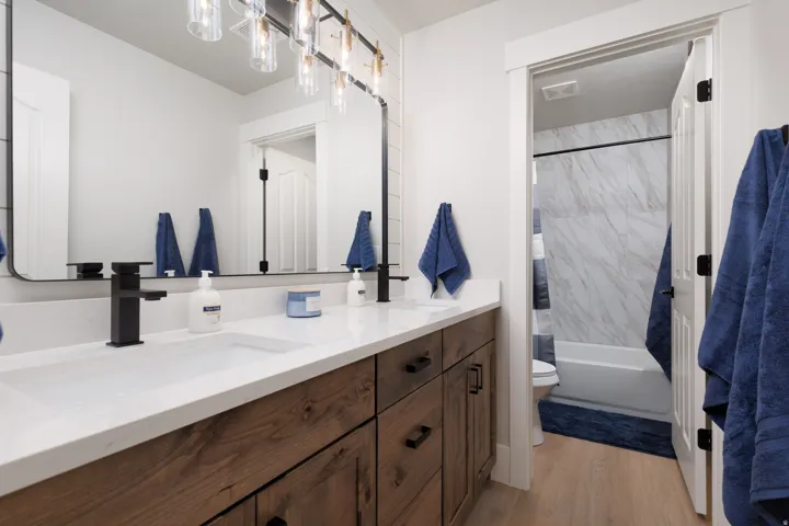 Dual vanity with wood-finish cabinetry, white countertops, and matte black fixtures