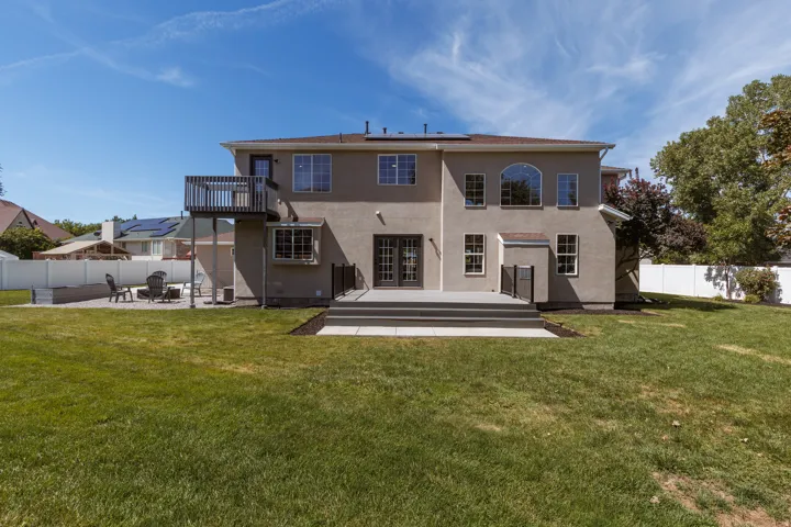 Expansive backyard featuring a manicured lawn, a multi-level deck, a second-story balcony, a paved patio, and a privacy fence