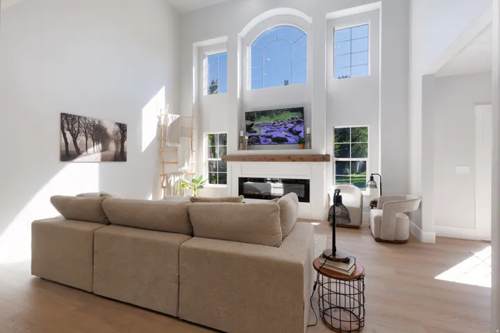 Two-story living area with high ceilings, an integrated fireplace, wood-finish flooring, and multiple windows including an arched upper window