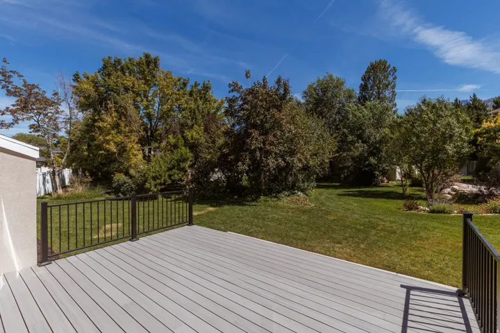 Expansive outdoor deck with gray composite decking and black metal railings, overlooking a large grassy yard with mature trees