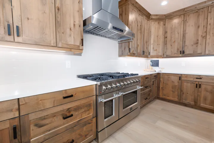 Wood-finish cabinetry with matte black hardware, white countertops, stainless steel professional-grade range, stainless steel range hood, and wood-finish flooring