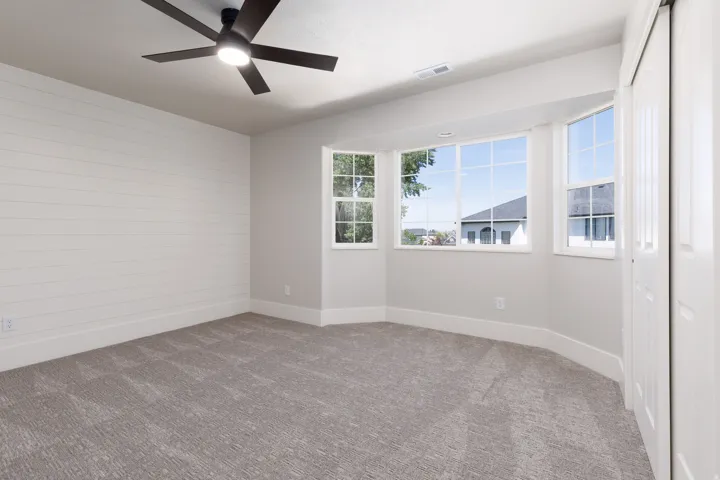 Recessed bay windows, ceiling fan with integrated lighting, textured carpeting, shiplap accent wall, and built-in closet with sliding doors