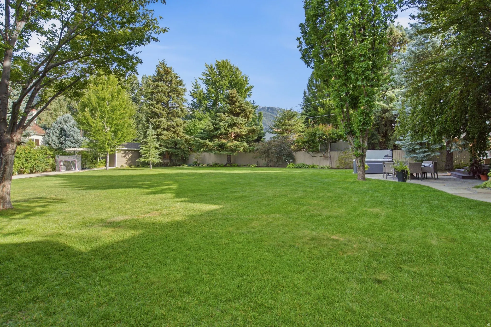 Expansive lawn with mature trees, a stone patio, and a built-in outdoor grill area
