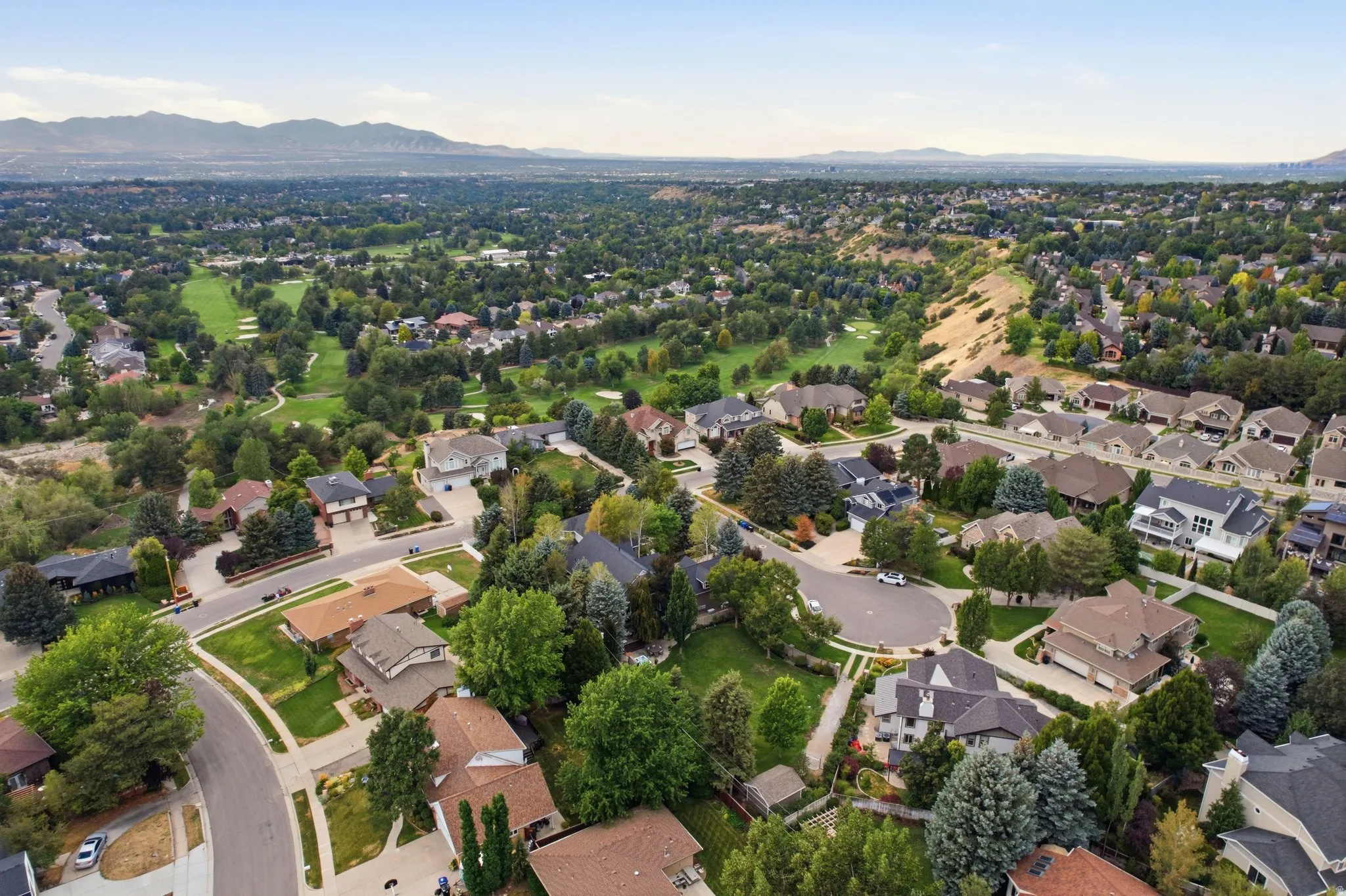Residential neighborhood with mature trees, a golf course, and distant mountains