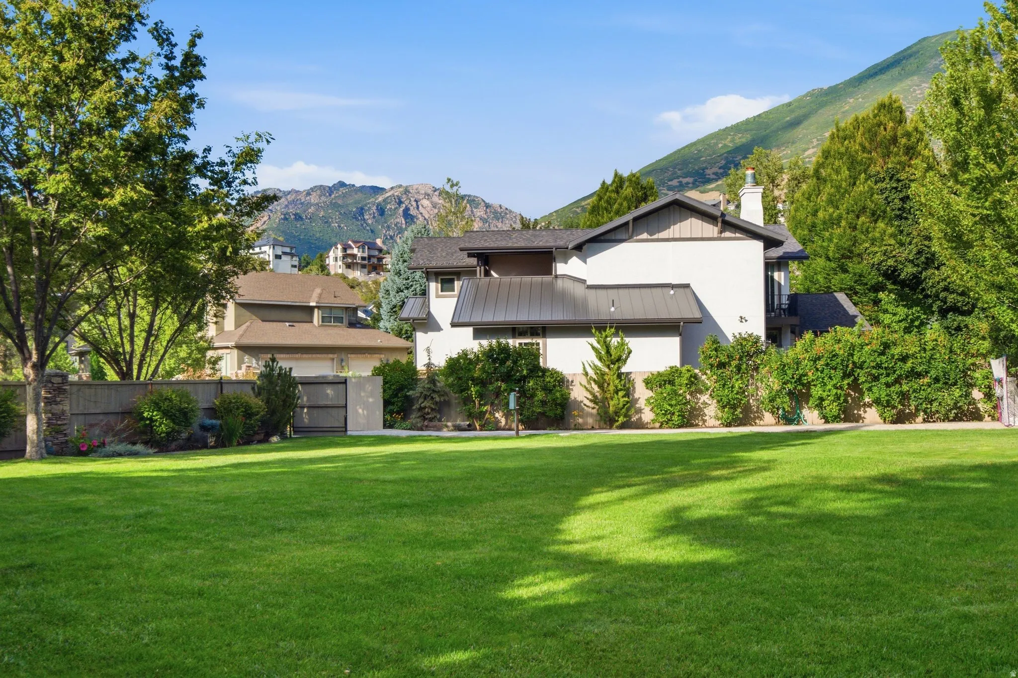 Expansive green lawn with mature trees, substantial fencing, and mountain scenery