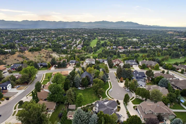 Expansive residential area featuring numerous dwellings, mature trees, paved streets, and mountainous backdrops