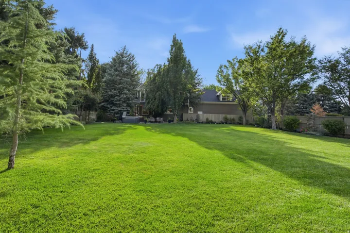 Expansive manicured lawn with mature perimeter trees and privacy fencing