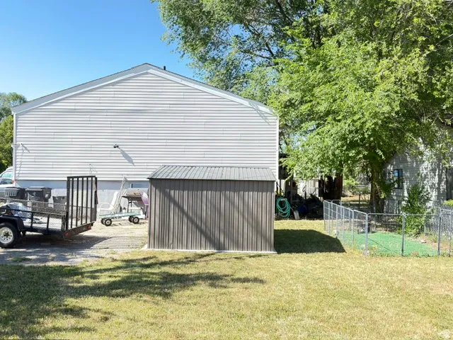 White siding exterior, metal storage shed, chain link fencing, mature trees, and a grassy area
