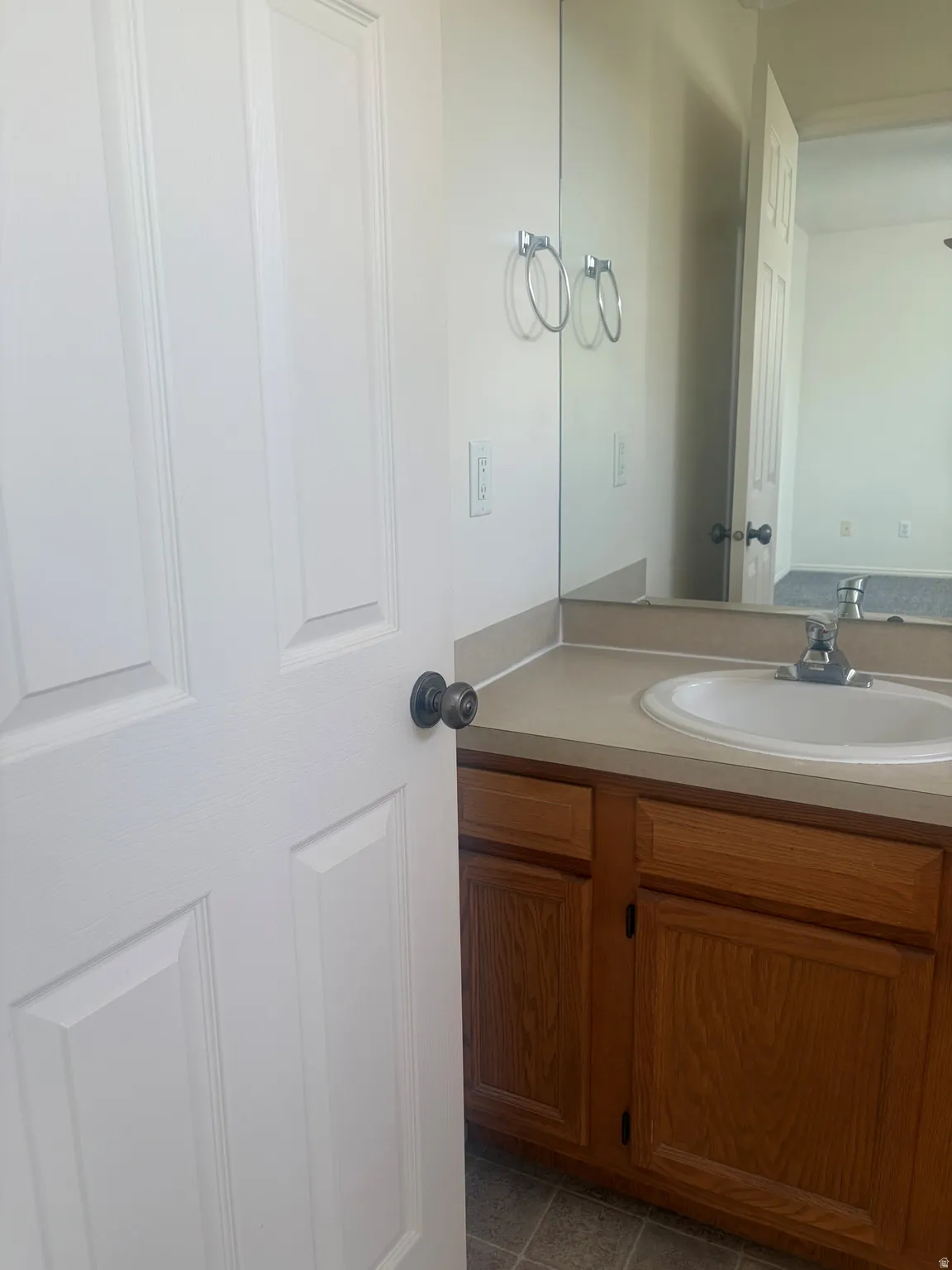 Vanity with a single basin sink, light-toned countertop, wood-finish cabinetry, and a full-width mirror