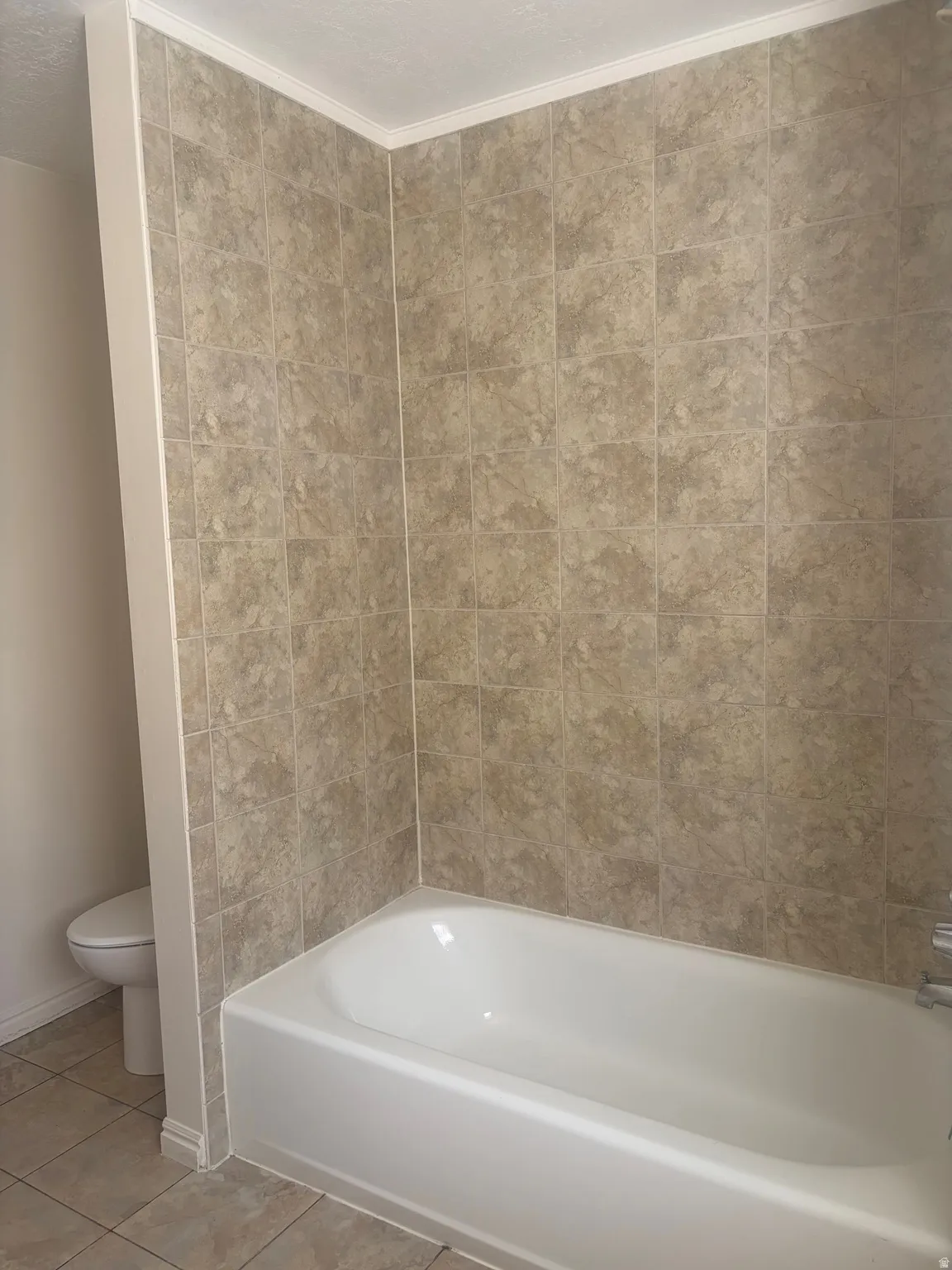 White bathtub with chrome fixtures, surrounded by neutral-toned wall tiles extending to the ceiling
